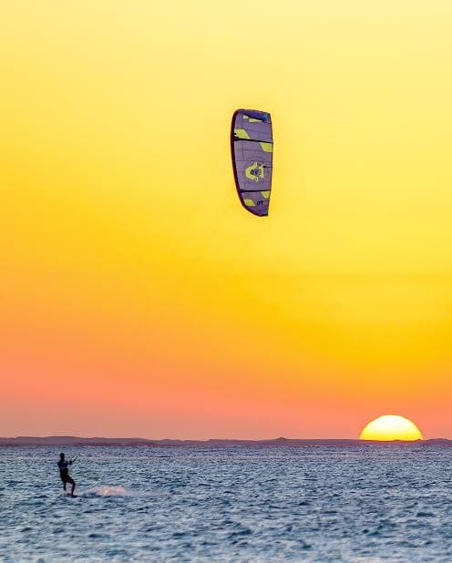 Kitesurfer riding a golden-hour wave in clear waters